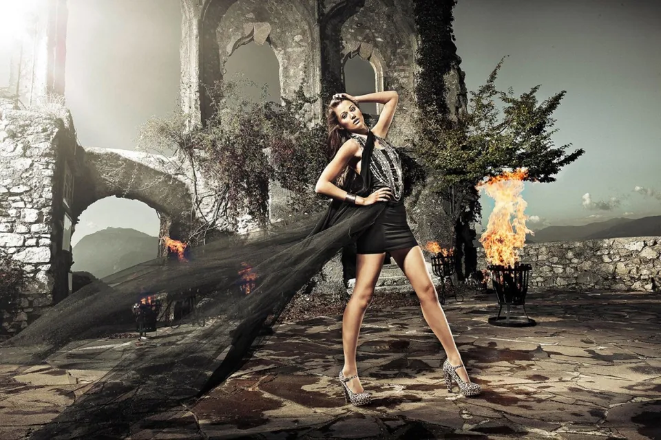 Model im schwarzen Kleid mit langer Schleppe vor einer Ruine mit Feuerschalen